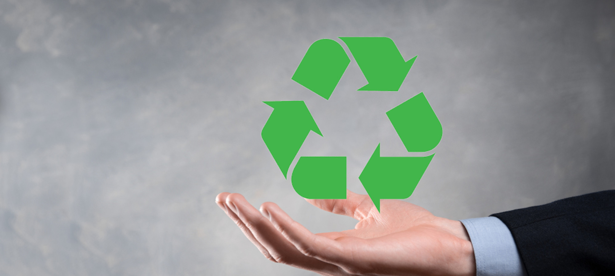 Empresario con traje sobre fondo oscuro sostiene un icono de reciclaje, con el cartel en las manos.